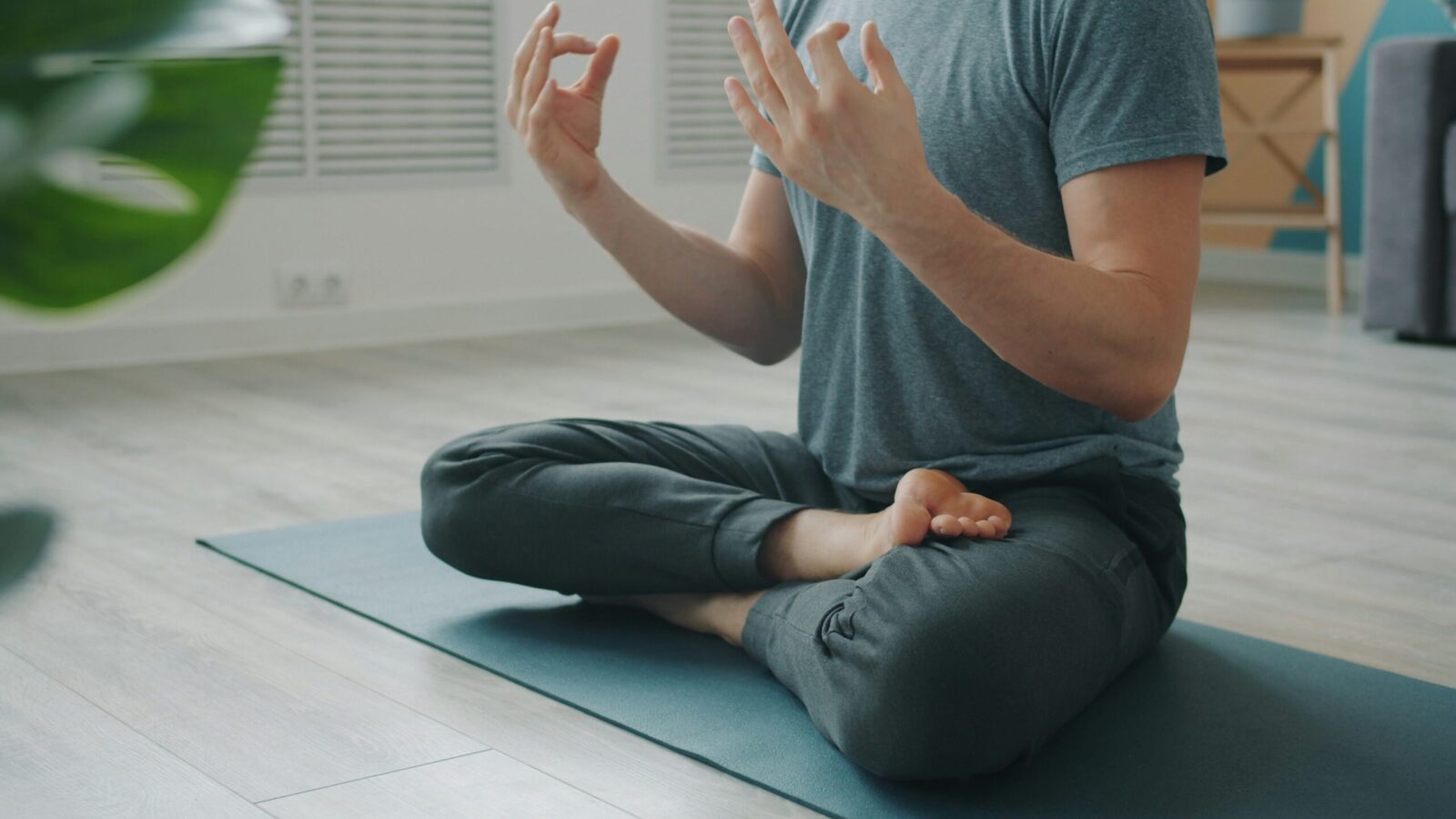 Person sitter i meditationsställning på yogamatta med händerna i mudra.